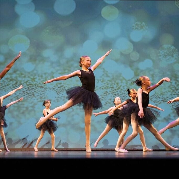 Young ballet dancers in black costumes performing on stage